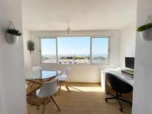 Um espaço moderno com área de refeições, espaço de trabalho e uma grande janela com vista para a cidade.