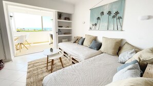 Une chambre avec un grand lit, une petite table et une chaise. Elle possède un balcon avec vue sur l’océan.