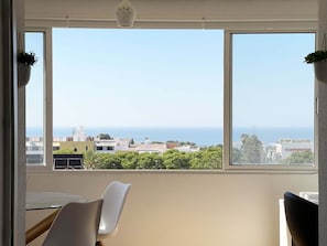 Quarto com uma grande janela que oferece vista para o mar e edifícios.