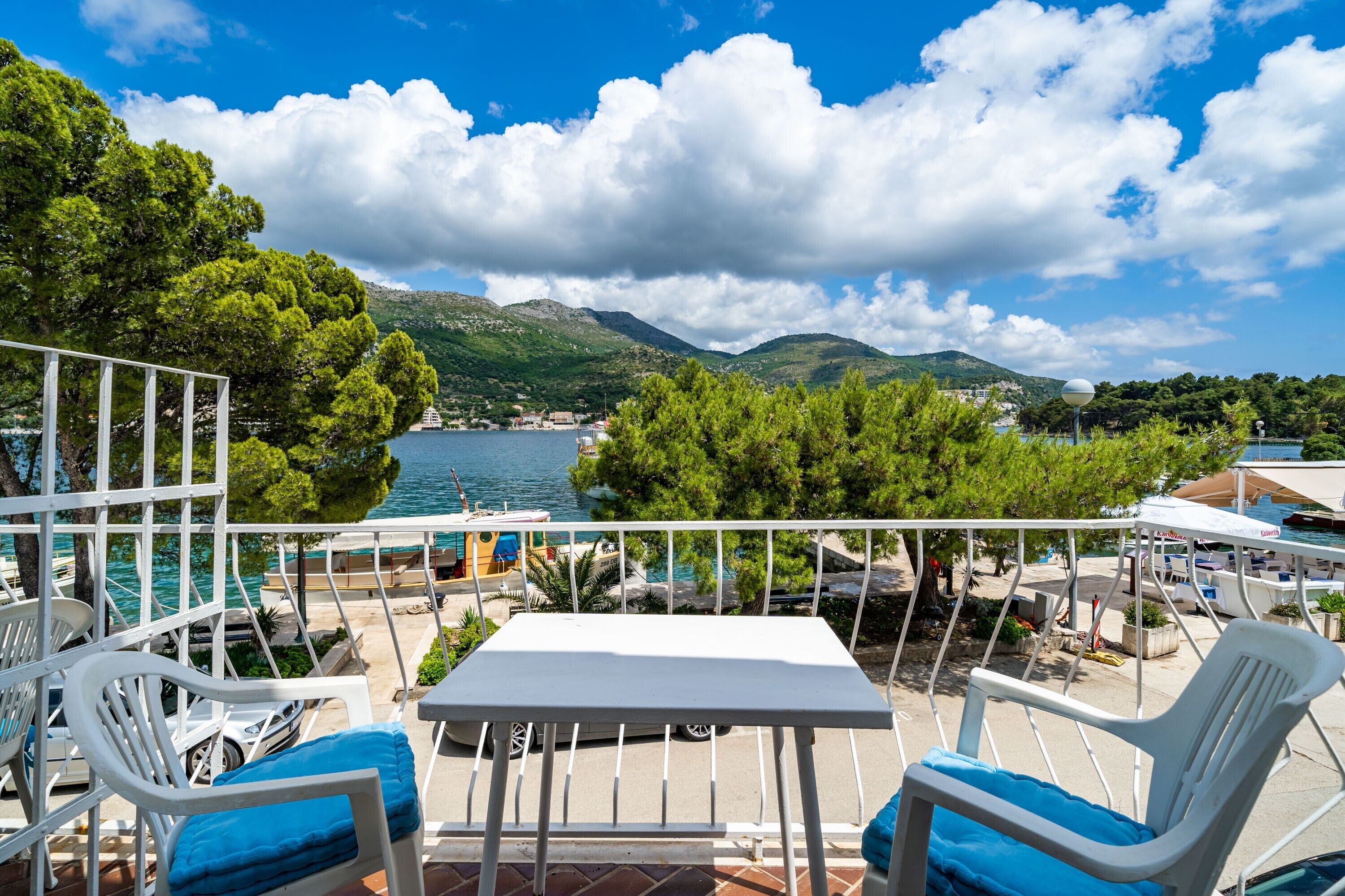 A terrace with white chairs and a table, overlooking a lake and mountains.