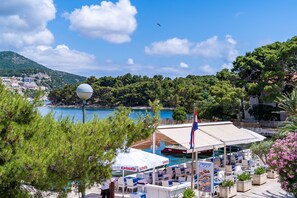 A coastal restaurant with outdoor seating overlooking the sea, a flag, and a view of the coastline. - Apartments Zarac - One Bedroom Apartment with Balcony and Sea View (Zaton)