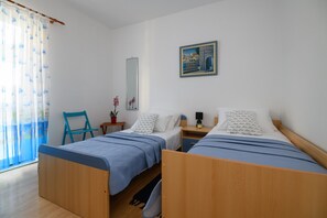 Una habitación con dos camas de madera, una silla, una mesita, un espejo y un cuadro en la pared.