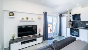 Ein modernes Wohnzimmer mit Flachbildfernseher, einer Couch und einer Küchenzeile inklusive Mikrowelle und Backofen.