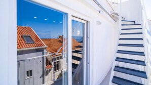 Ein modernes Gebäude mit einer Glastür, die auf einen Balkon führt, einer Treppe und Blick auf ein rotes Ziegeldach.