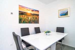Una sala de conferencias con una mesa blanca, cuatro sillas negras, un florero y dos cuadros en la pared.