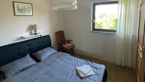 Une chambre à coucher avec un lit, une chaise, une fenêtre et un luminaire suspendu.