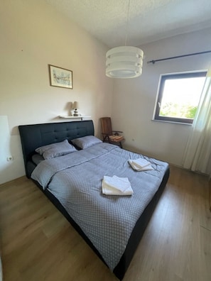 Une chambre à coucher comprenant un lit, une table de chevet, une chaise, une fenêtre et un luminaire au plafond.
