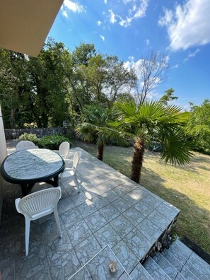 Eine Terrassengruppe mit Tisch und Stühlen, umgeben von einem Garten mit Palmen und einer Steinmauer.