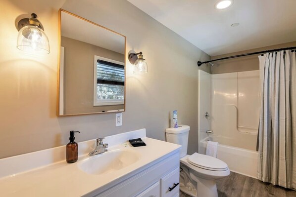 Un baño con lavamanos, espejo, inodoro y ducha blanca.