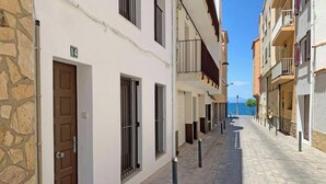A narrow street lined with multi-story buildings, featuring stone walls, balconies, and a clear view of the sea. - Casa del Pescadores - Four Bedroom House, Sleeps 8 (L'Escala)
