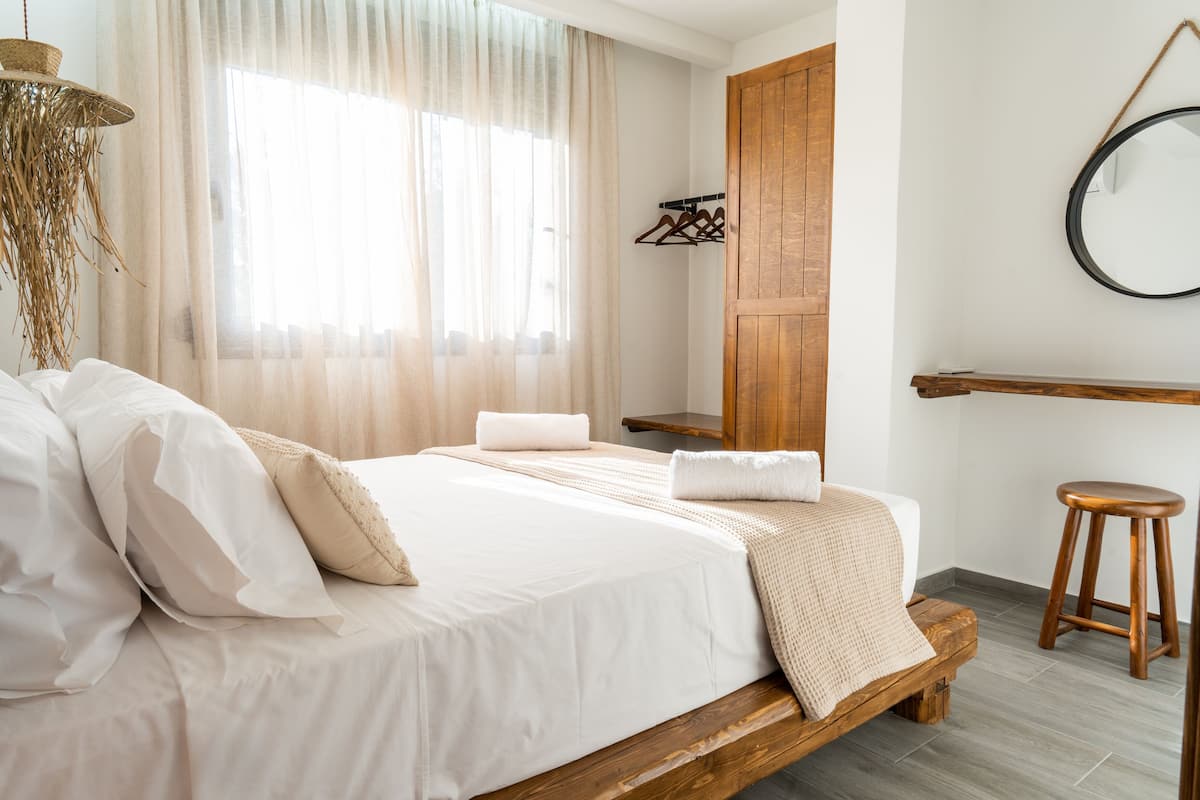 Een slaapkamer met een houten bed, een hanglamp, een spiegel en een houten kruk.