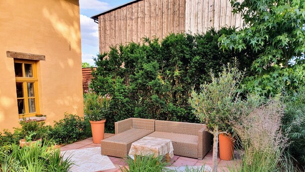 A patio with wicker furniture, a potted plant, and a wooden wall. - Boutique vacation apartment Westera on the sunny hill near the Baltic Sea! (Carinerland)