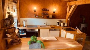 A rustic kitchen with wooden beams, a brick accent wall, a central island with a cutting board, and a sink. - Boutique vacation apartment Westera on the sunny hill near the Baltic Sea! (Carinerland)