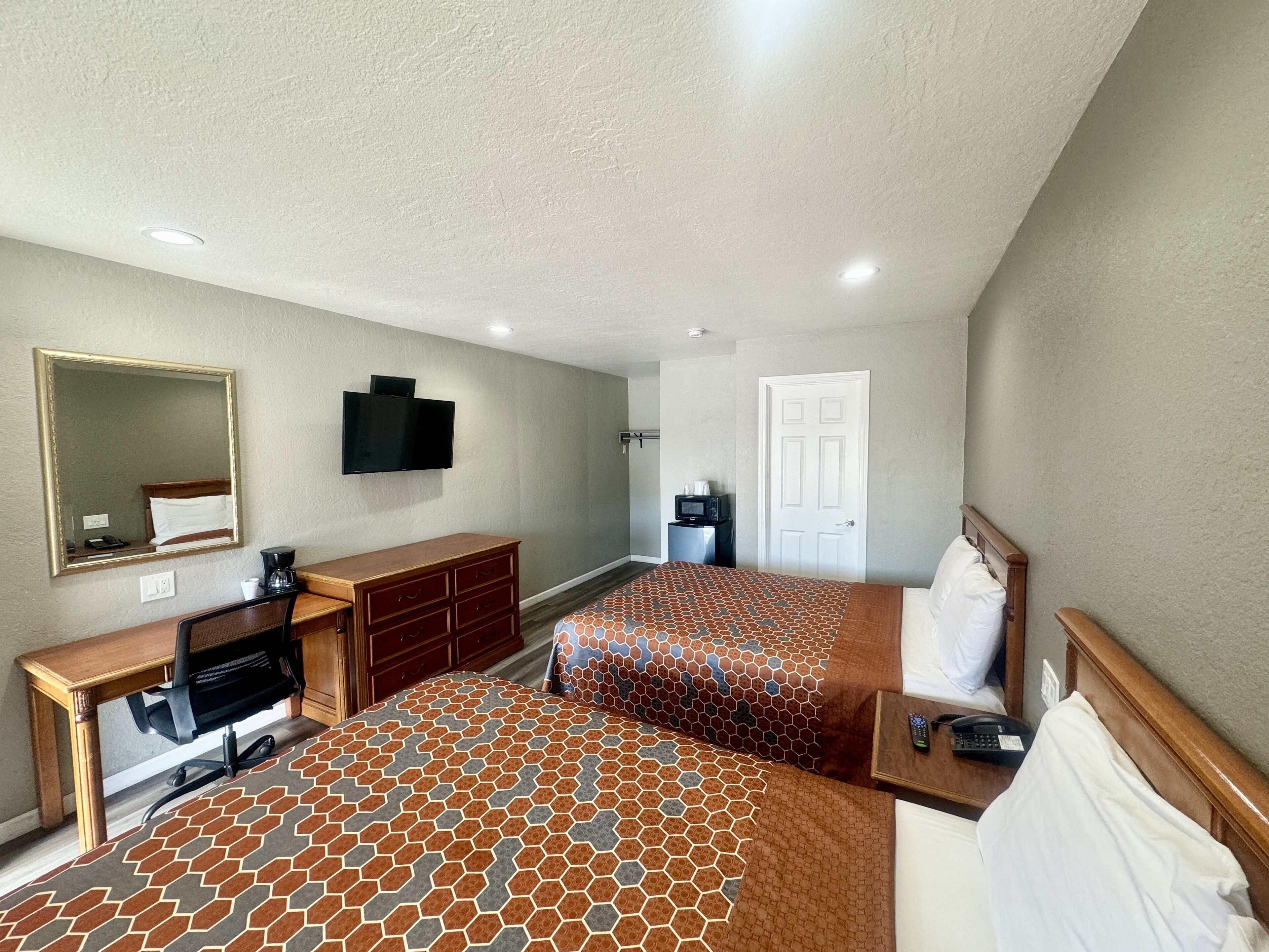 Une chambre d’hôtel avec deux lits, un bureau avec une chaise, une télévision et une porte.