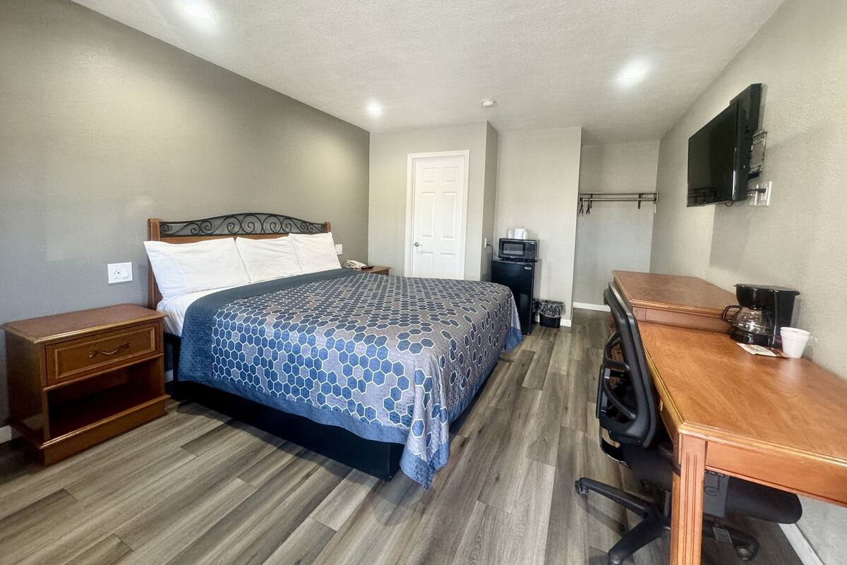 A bedroom with a bed, a desk, a chair, a television, and a coffee maker.