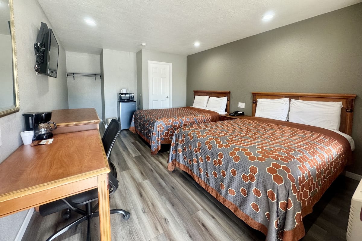A hotel room with two beds, a desk, a coffee maker, a microwave, and a TV.
