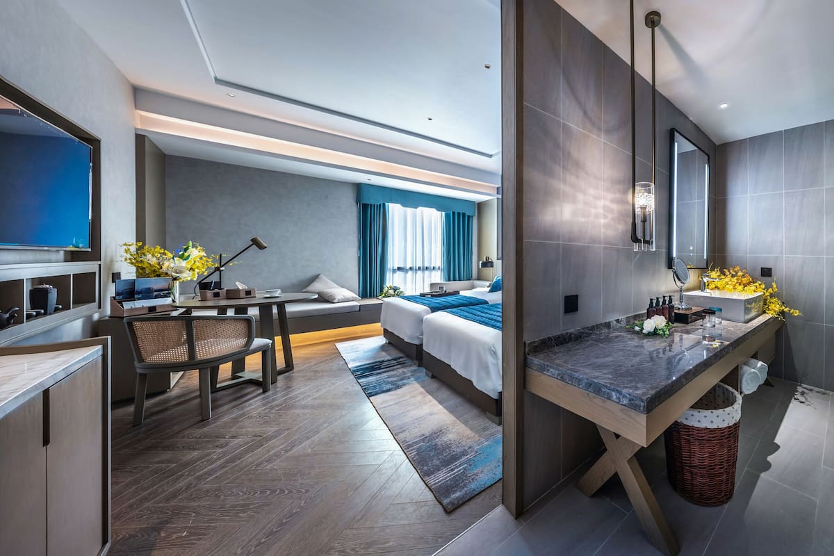 Habitación de hotel moderna con sofá, cama, escritorio y baño con ducha de vidrio.