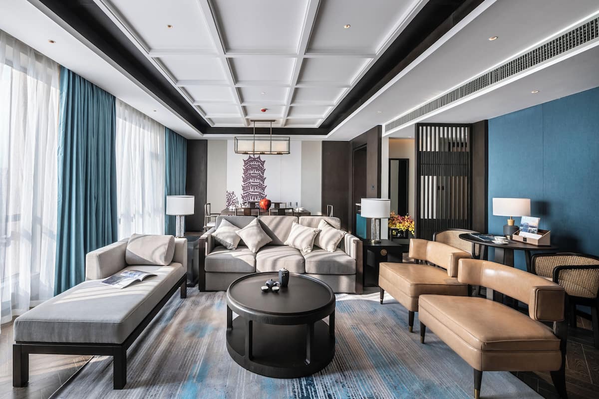 Una habitación de hotel moderna con sofá, sillones, una mesa de centro y una mesa de comedor.