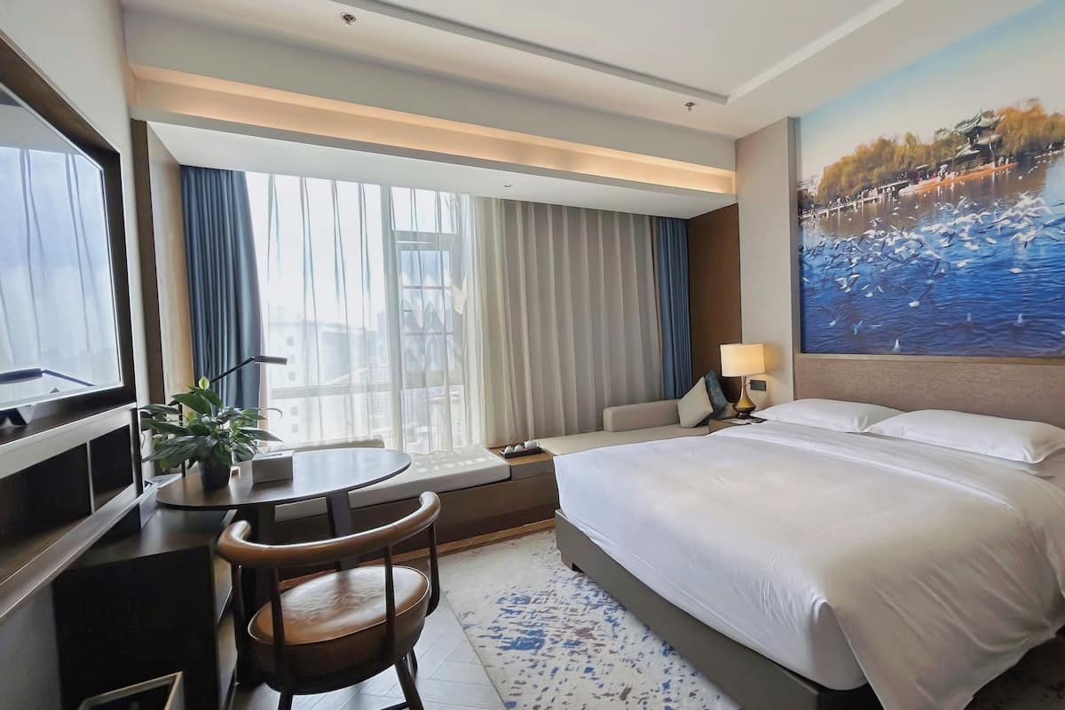 Habitación de hotel con una cama grande, un escritorio con silla, un televisor y un cuadro de aves sobre el agua en la pared.