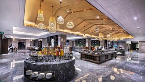 Un moderno vestíbulo de hotel con un mostrador de recepción de mármol, varias zonas de bar y lámparas colgantes.