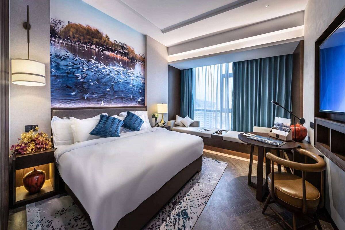 Una habitación de hotel moderna con una cama grande, una zona de estar con vistas y una mesa de comedor.