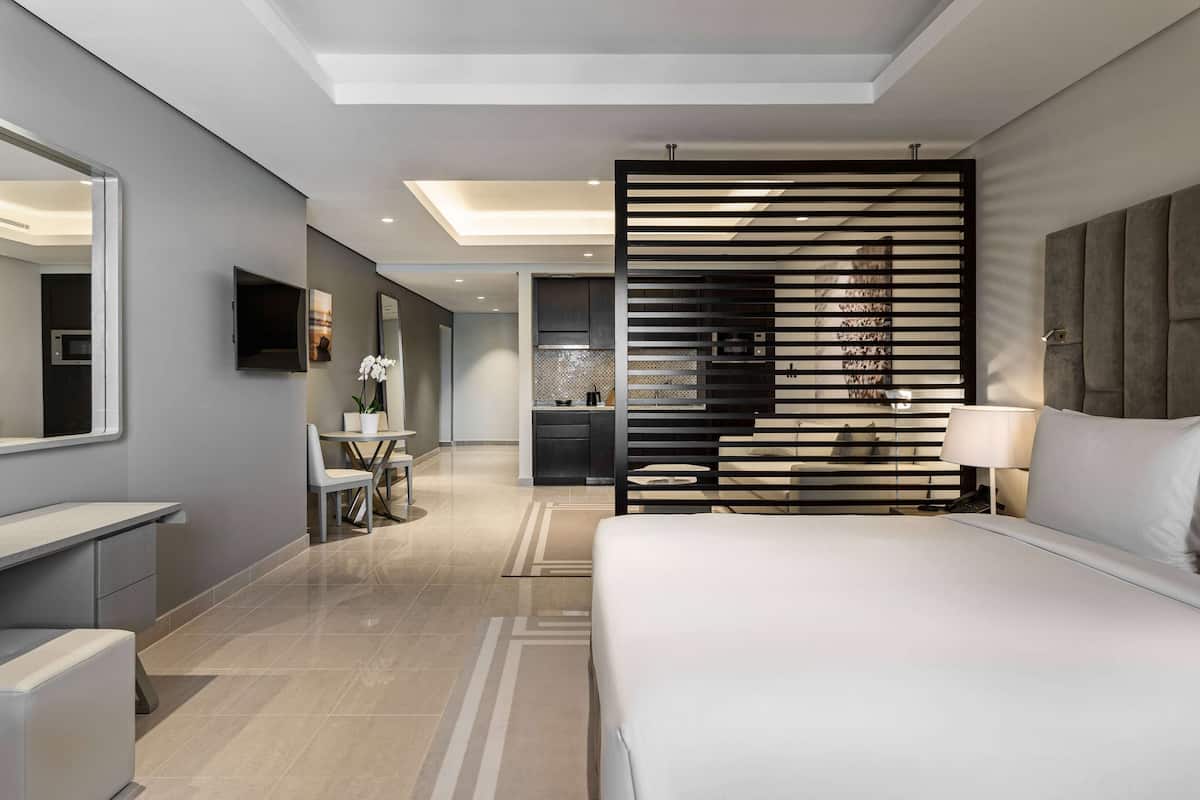 A modern hotel room with a large bed, a desk, a chair, a TV, and a bathroom visible through an open door.