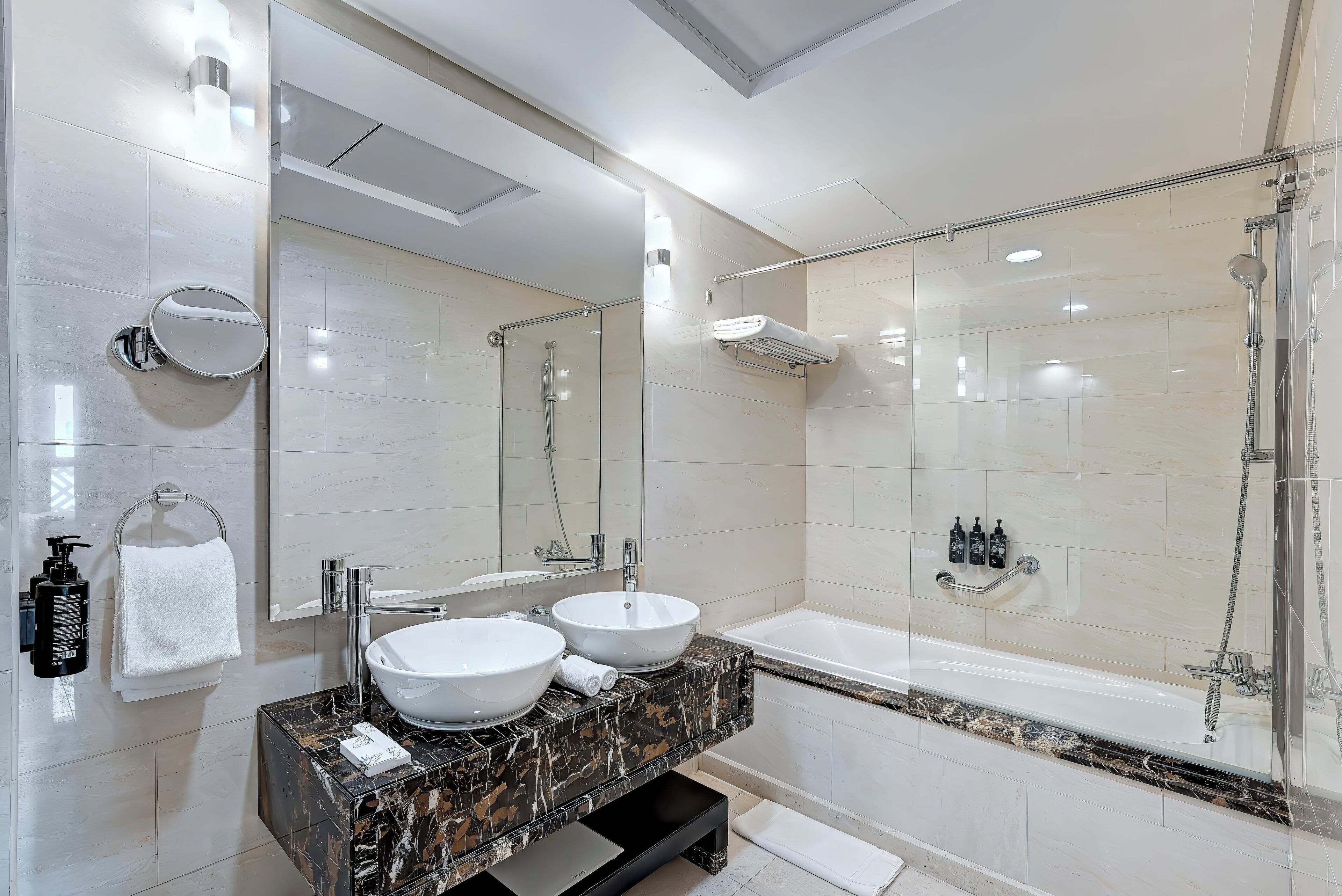 A modern bathroom with two sinks, a large mirror, a glass-enclosed shower, and a bathtub.