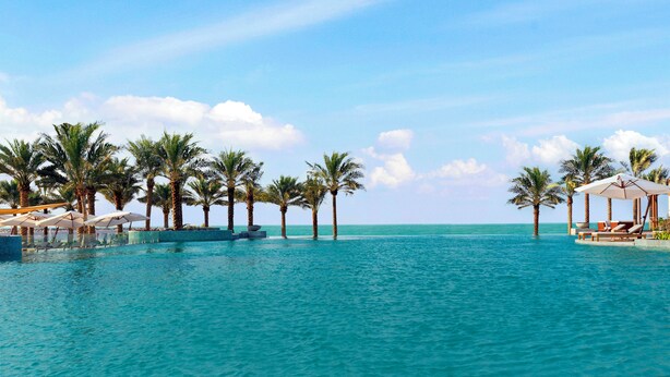 A resort pool with palm trees and lounge chairs. - Wyndham Residences The Palm (Dubai)