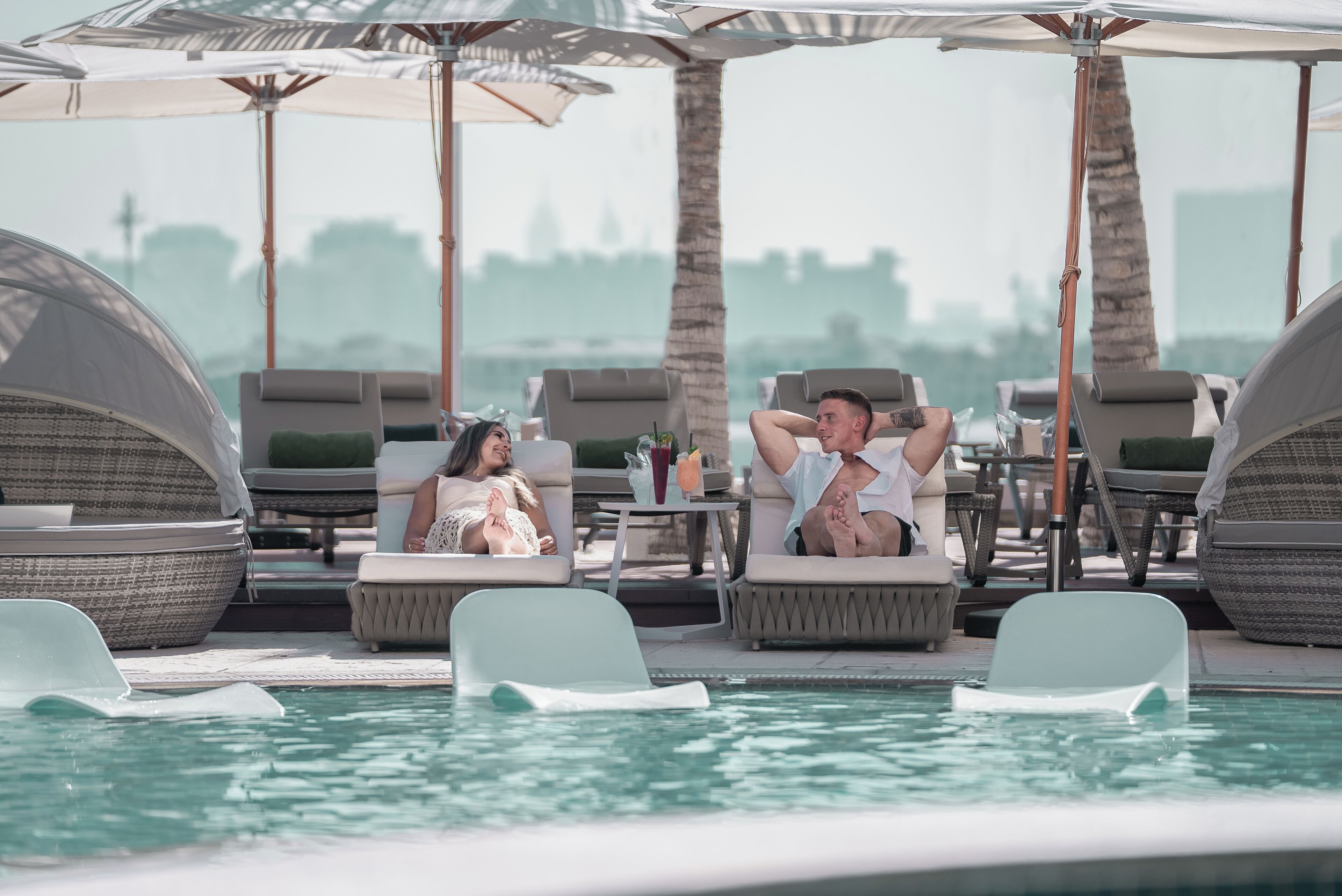 Zona junto a la piscina con sillones, sombrillas y vista al agua.