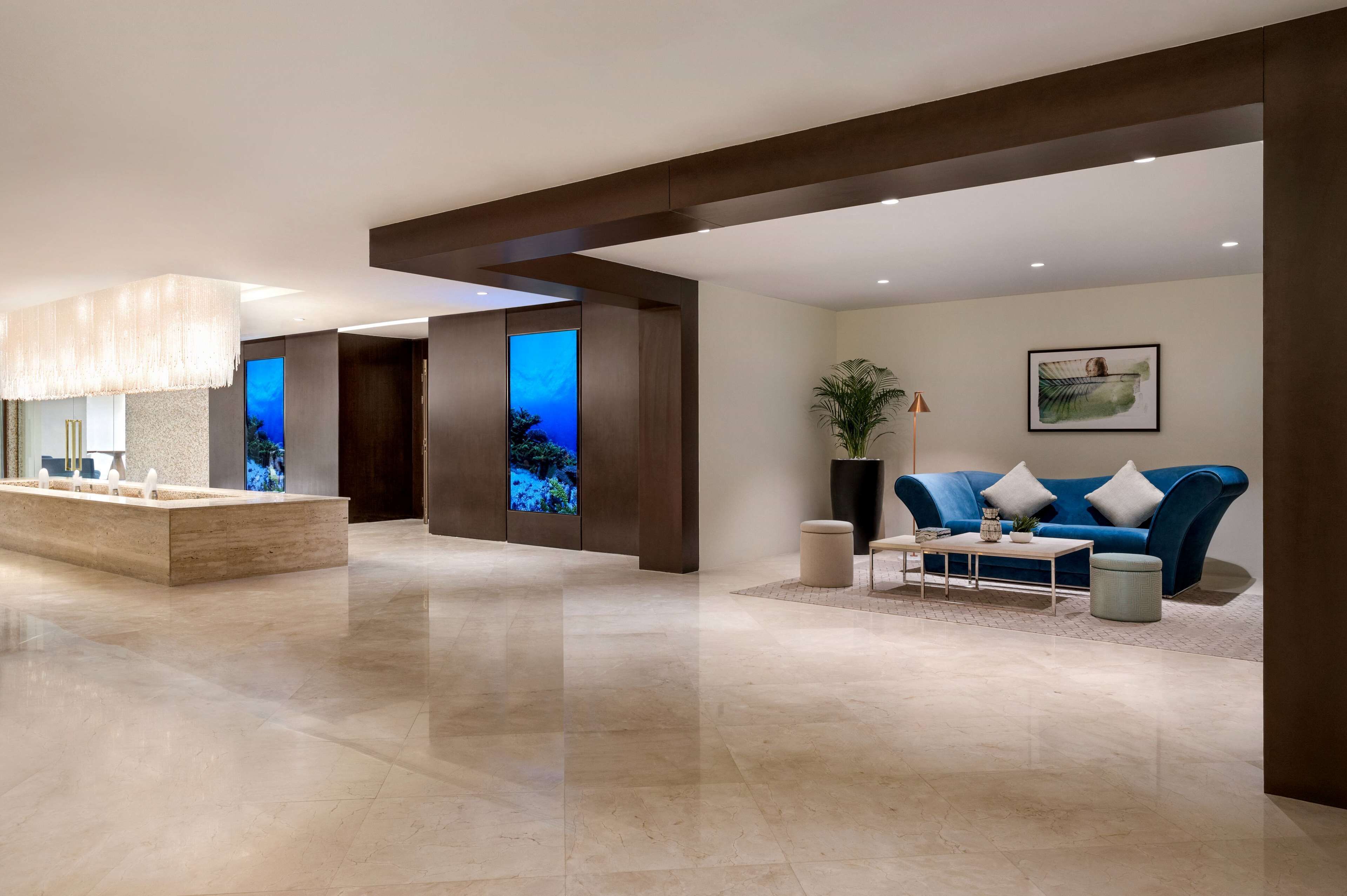 Een moderne lobby met een receptiebalie, een blauwe bank en een groot digitaal scherm waarop een natuurscène wordt getoond.