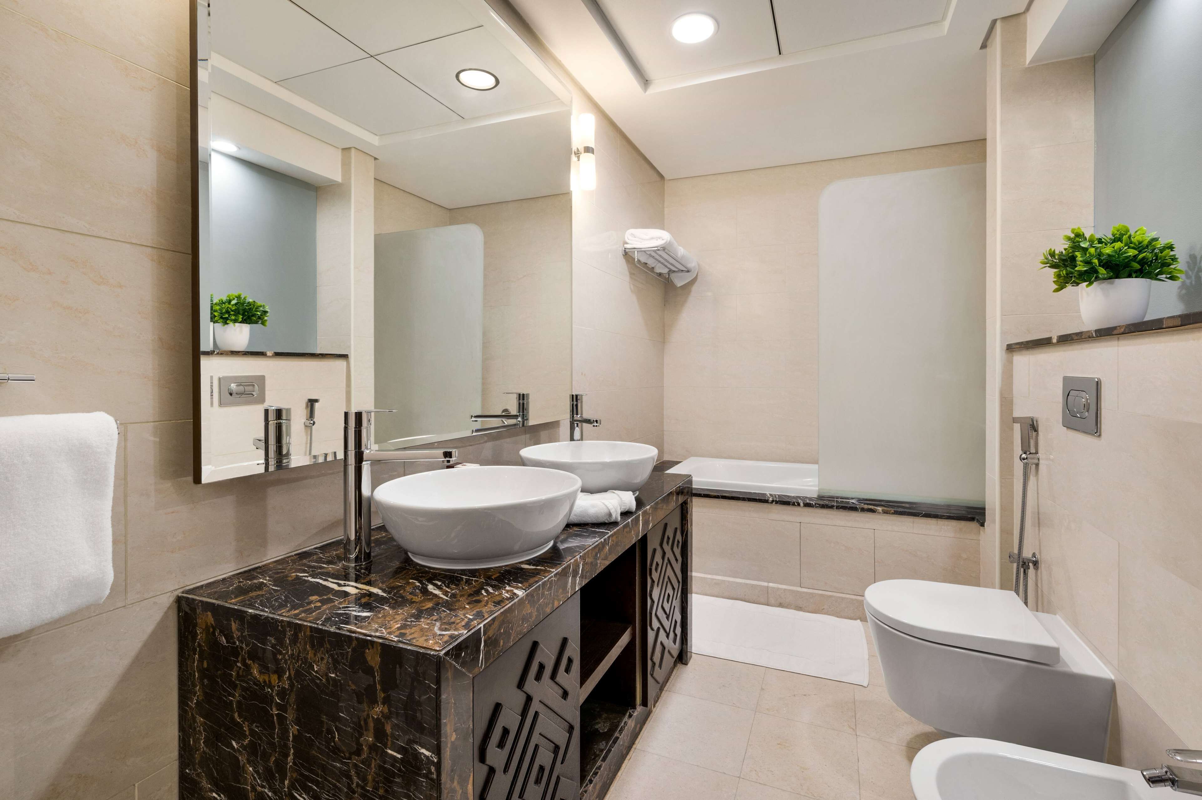 A modern bathroom with a marble vanity, two sinks, a large mirror, a toilet, and a shower area.