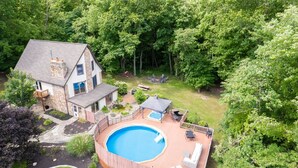 Une maison avec une piscine dans le jardin, un patio couvert et une cheminée en pierre.