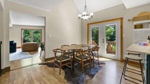 Un vaste espace dédié à la salle à manger, avec une table et des chaises en bois, un lustre et une vue sur l’extérieur grâce à de grandes portes coulissantes.