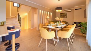 A dining area with a wooden table set for four, surrounded by yellow chairs. A modern pendant light hangs above the table. - Villa MAGNIFICA with pool (Pinezići)