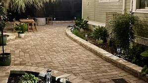 Un'area patio lastricata con un vialetto curvo, mobili da esterno e luci a tenda.