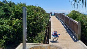 Ein hölzerner Steg führt zum Strand, mit einem Stuhl und einer Person in der Ferne.