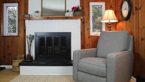 A living room with a fireplace, a grey armchair, a lamp, and a clock on the wall.
