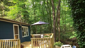 A wooden deck with outdoor furniture, a potted plant, and a view of a forested area.