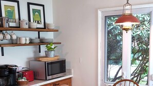 A kitchen with wooden cabinets, a microwave, a kettle, and a hanging light fixture.