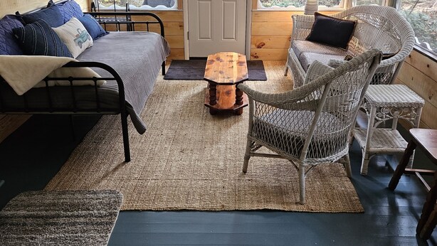 A cozy room with a bed, a sofa, a wicker chair, a small wooden table, and a door leading outside.