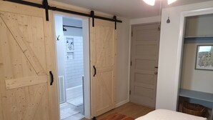 A bedroom with a wooden bed, a sliding door closet, and a white tiled bathroom visible through the door.
