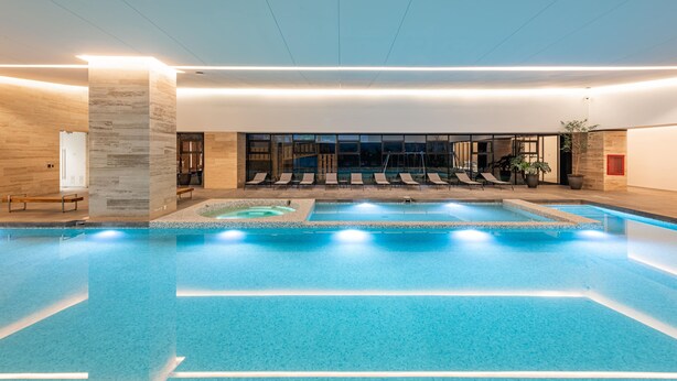 A large indoor swimming pool with multiple lounge chairs and a small hot tub area. - Nido x Neuchatel Polanco (Mexico City)