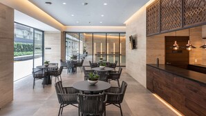 A modern indoor dining area with round tables and wicker chairs, large windows, and a wooden counter with pendant lighting. - Nido x Neuchatel Polanco (Mexico City)
