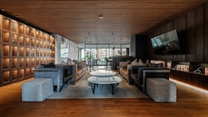 A modern living room with a wooden ceiling, a large TV, and a seating area with sofas and ottomans. - Nido x Neuchatel Polanco (Mexico City)