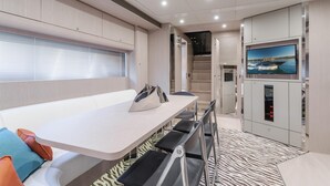 Un interior moderno con zona de comedor, televisor montado en la pared y escalera que lleva a otra habitación.