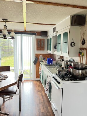 A kitchen with wooden cabinets, a stove, and a dining table with chairs. - Island-getaways cottage rental and cod fishing. We do island tours upon estuary (York Harbour)