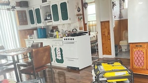 A kitchen with white cabinets, a stove, and a sink. There is a dining table with chairs and a suitcase on the floor. - Island-getaways cottage rental and cod fishing. We do island tours upon estuary  (York Harbour)