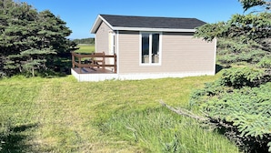 A single-story house with a deck, surrounded by a grassy field and trees. - Island-getaways cottage rental and cod fishing. We do island tours upon estuary  (York Harbour)