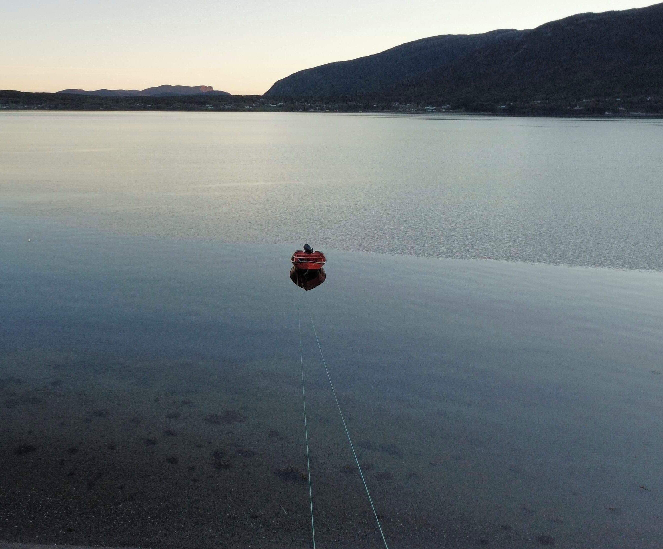 Een rustig meer met een boot die midden in het water ligt aangemeerd, omringd door bergen.