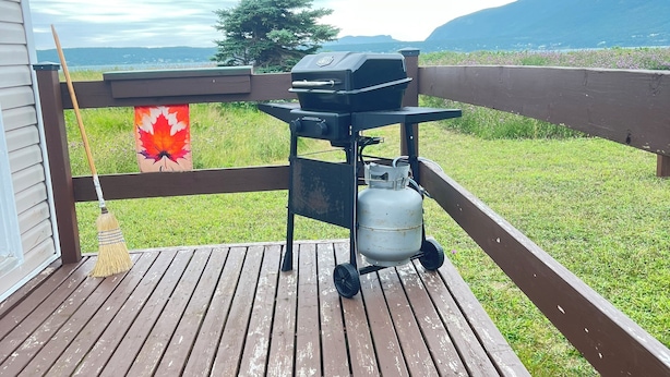 A wooden deck with a barbecue grill and propane tank. - Island-getaways cottage rental and cod fishing. We do island tours upon estuary  (York Harbour)